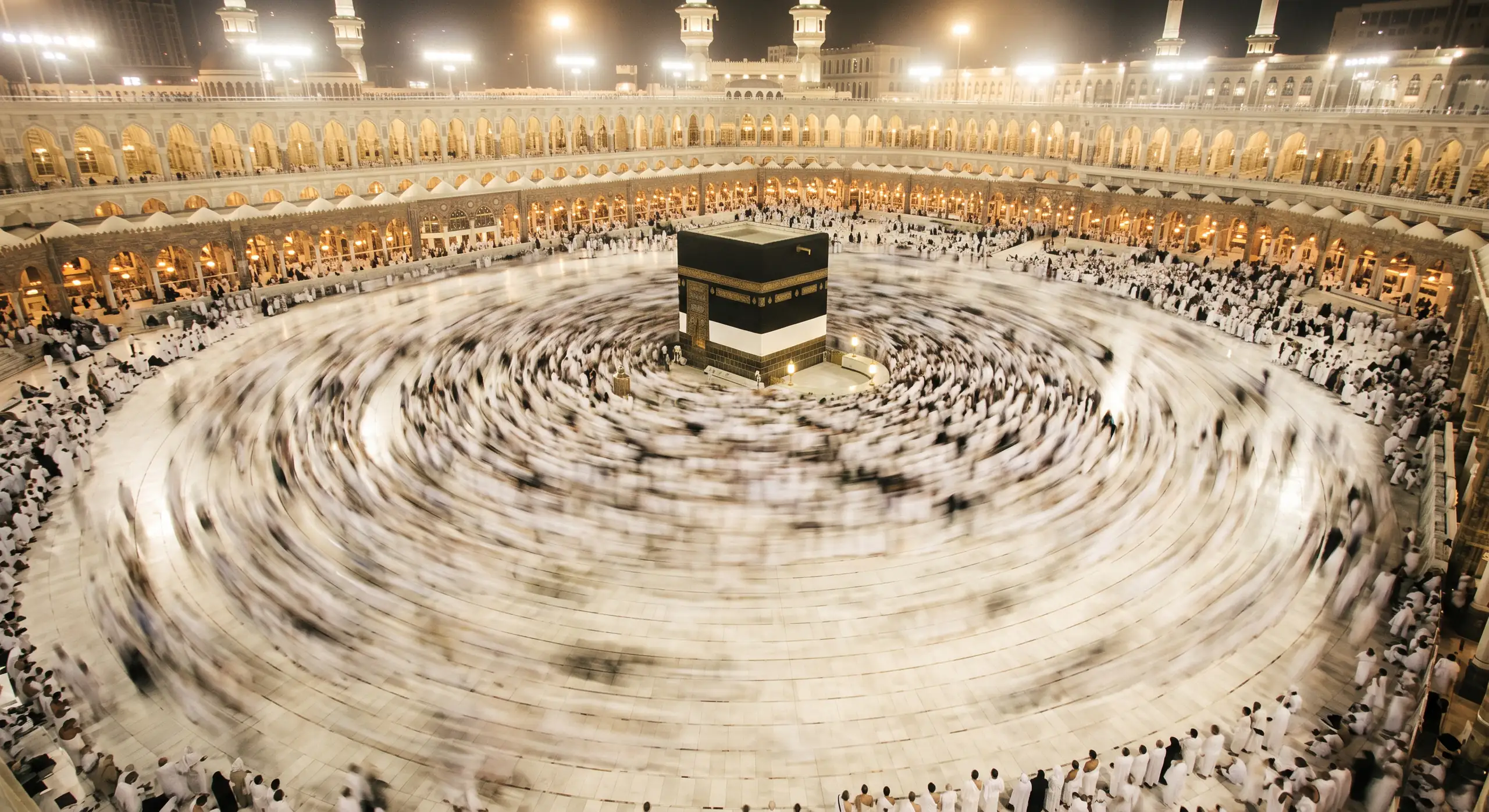 Ribuan jamaah melakukan thawaf mengelilingi Ka'bah di Masjidil Haram pada malam hari, difoto dari ketinggian dengan rana lambat sehingga gerak kerumunan tampak melingkar