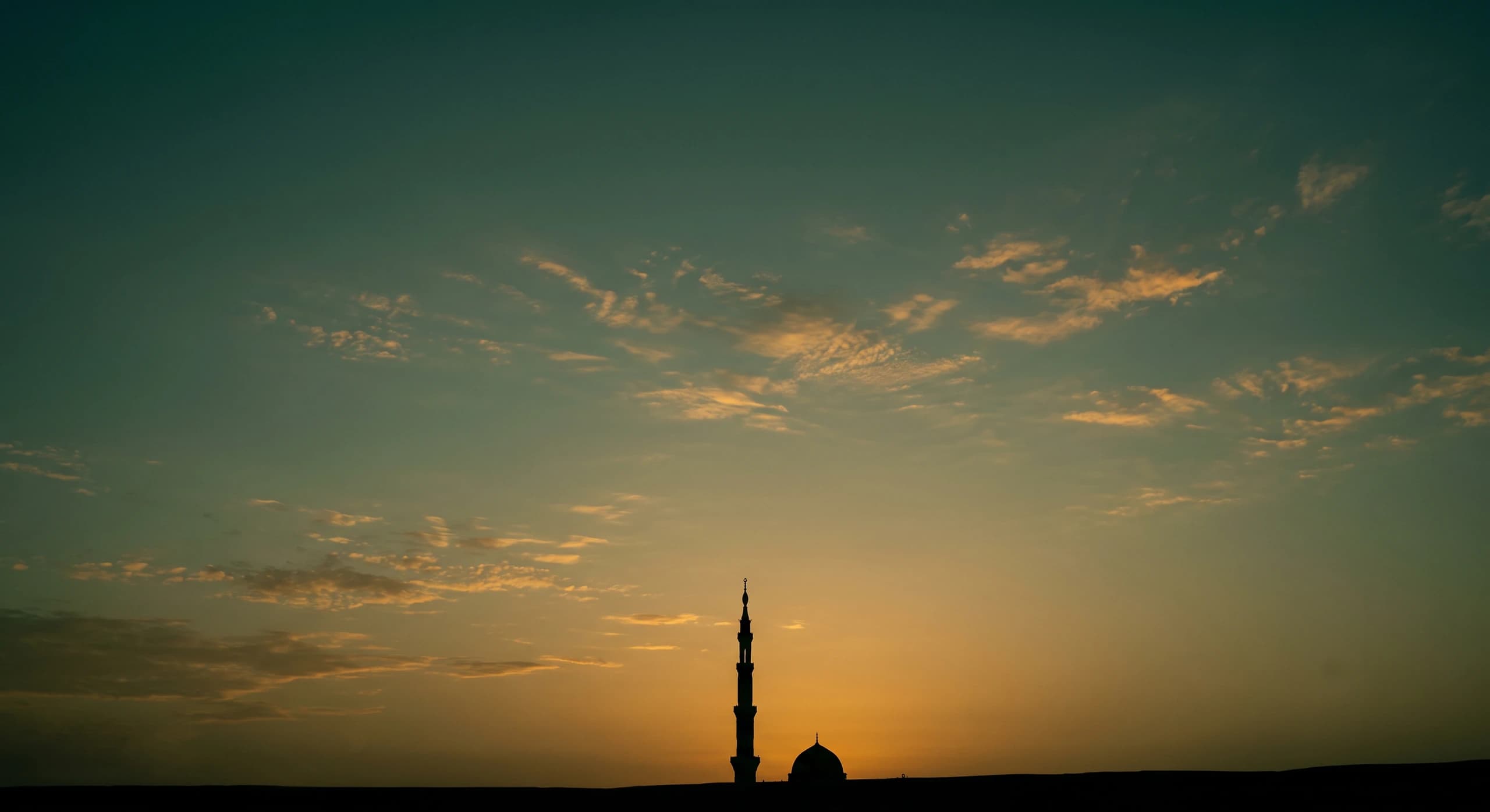 Langit senja Madinah bergradasi jingga ke biru, dengan siluet menara dan kubah masjid di garis cakrawala
