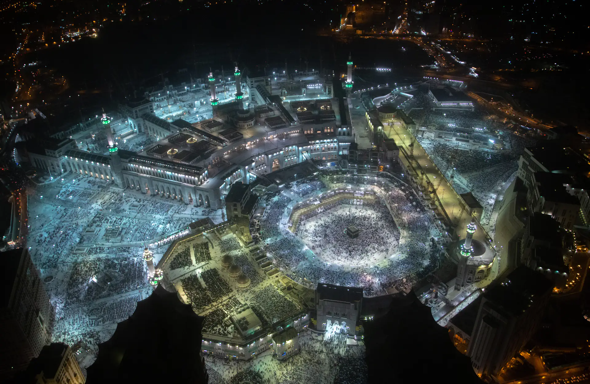 Masjidil Haram pada malam hari difoto dari udara — Ka'bah di tengah dikelilingi lingkaran jamaah yang sedang thawaf, dengan pelataran dan menara masjid bermandi cahaya