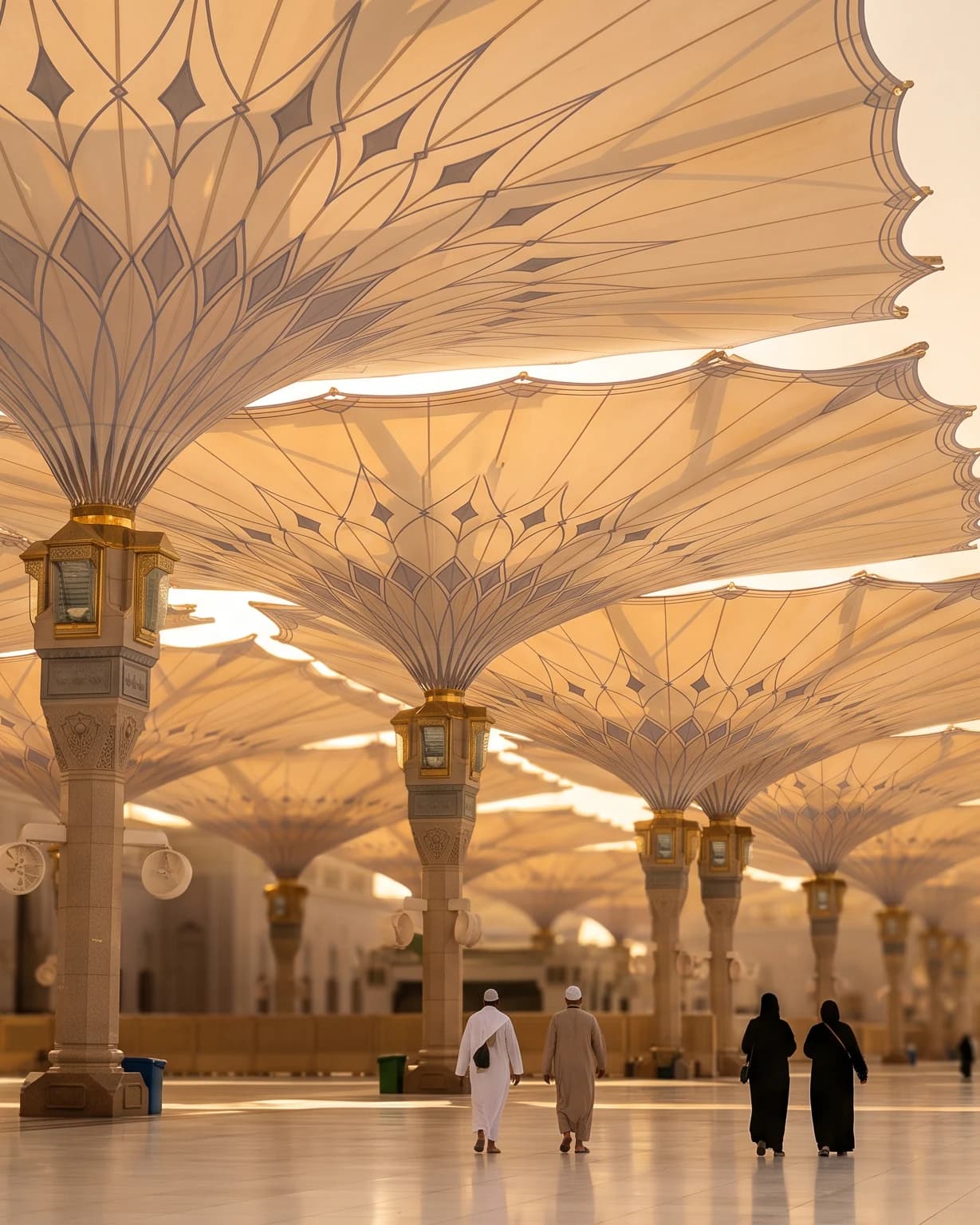 Payung-payung raksasa di halaman Masjid Nabawi terbuka saat golden hour, beberapa jamaah berjalan menjauh di bawahnya